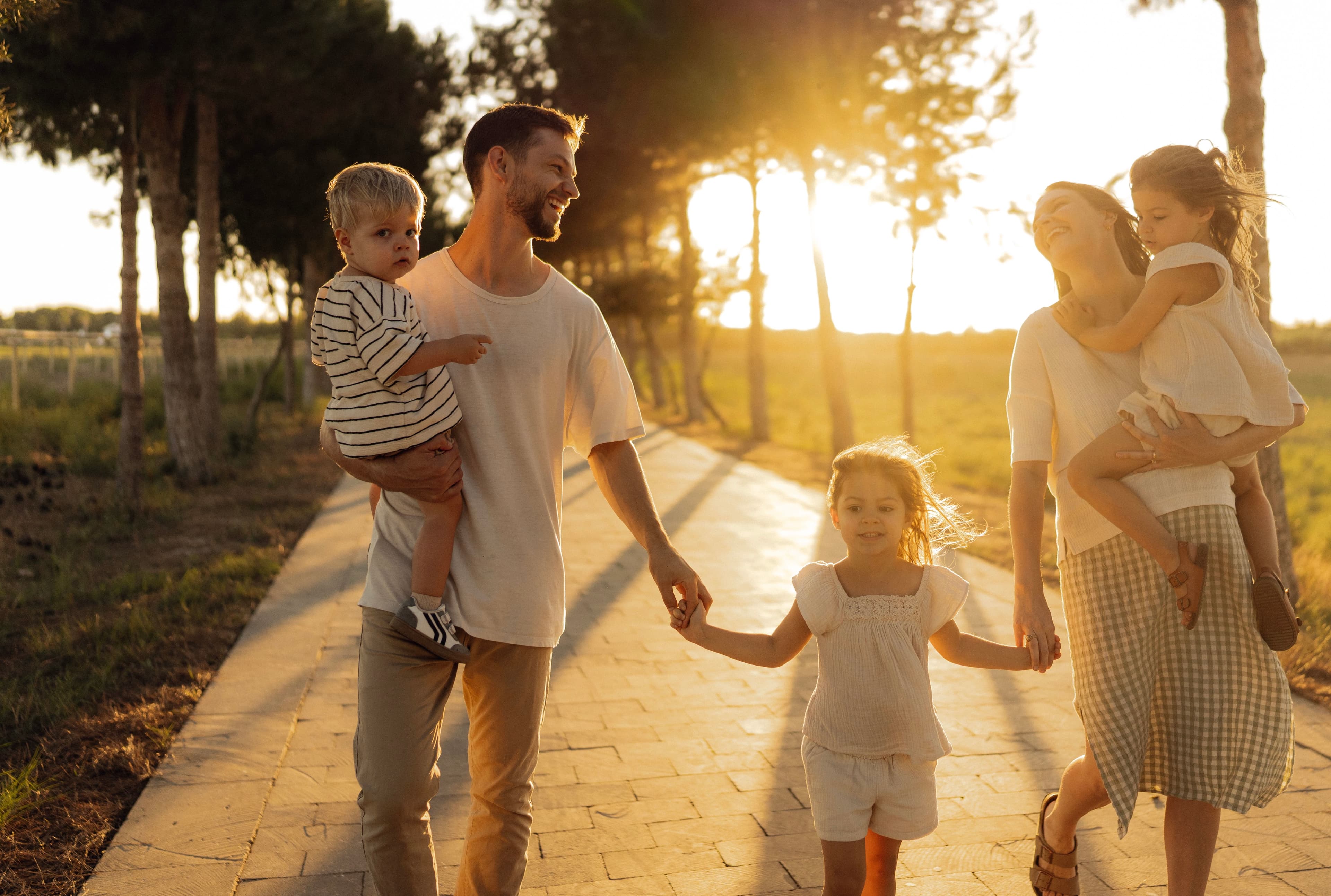 Familia feliz caminando por un sendero arbolado bajo la luz dorada de un atardecer.