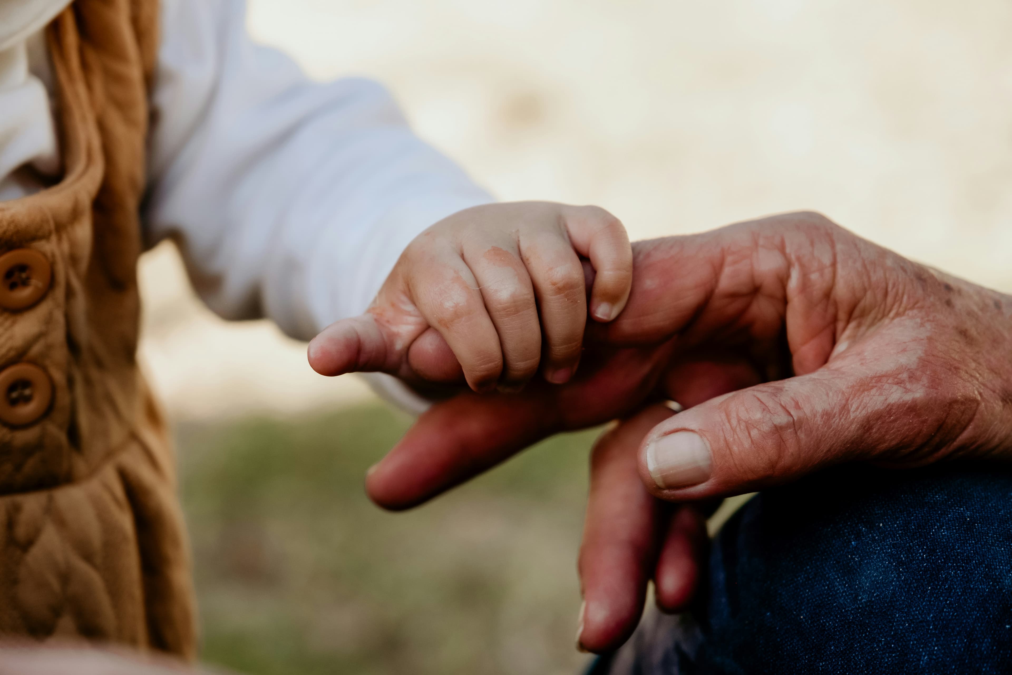 La mano pequeña de un niño sostiene con ternura el dedo arrugado de un anciano.